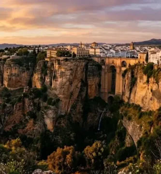 Vista panorâmica do desfiladeiro de Ronda e da Puente Nuevo ao pôr-do-sol, com o casario branco no topo das arribas rochosas.