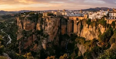 Vista panorâmica do desfiladeiro de Ronda e da Puente Nuevo ao pôr-do-sol, com o casario branco no topo das arribas rochosas.